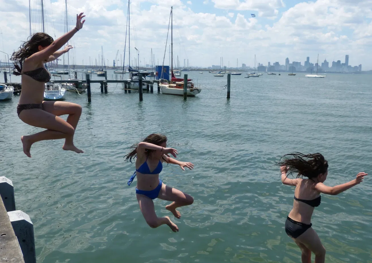 Children jumping off the Williamstown pier with the Melbourne skyline in the distance